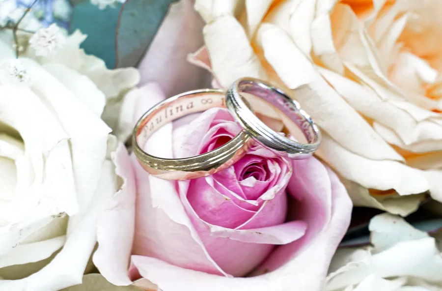 Zwei Eheringe liegen auf cremefarbenen und rosa Rosen