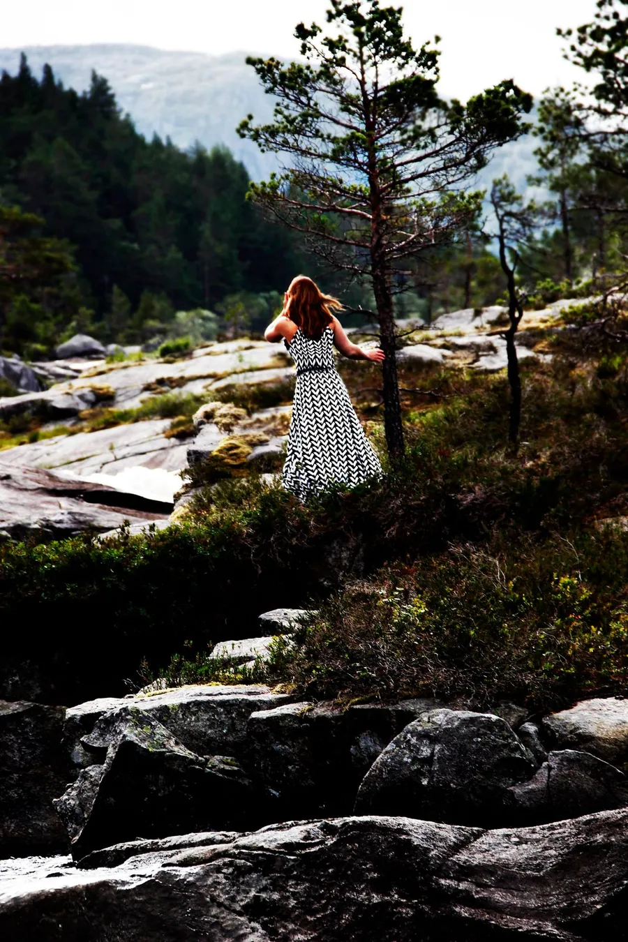 Eine Frau im gepunkteten Kleid geht über Felsen in einer weiten Landschaft