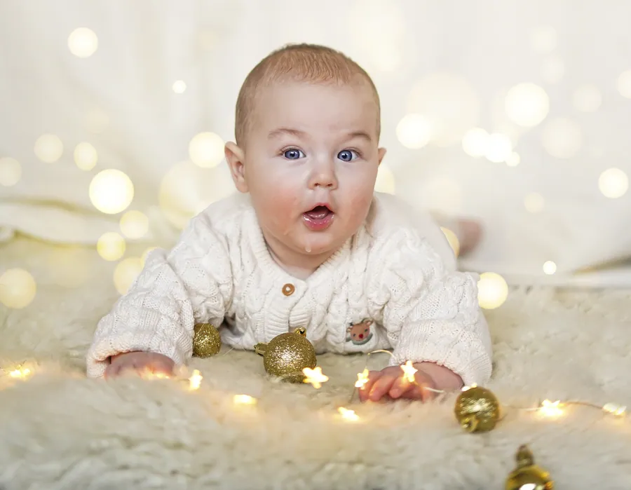 Ein Baby in heller Strickjacke liegt auf einem Fell zwischen goldenen Lichtern