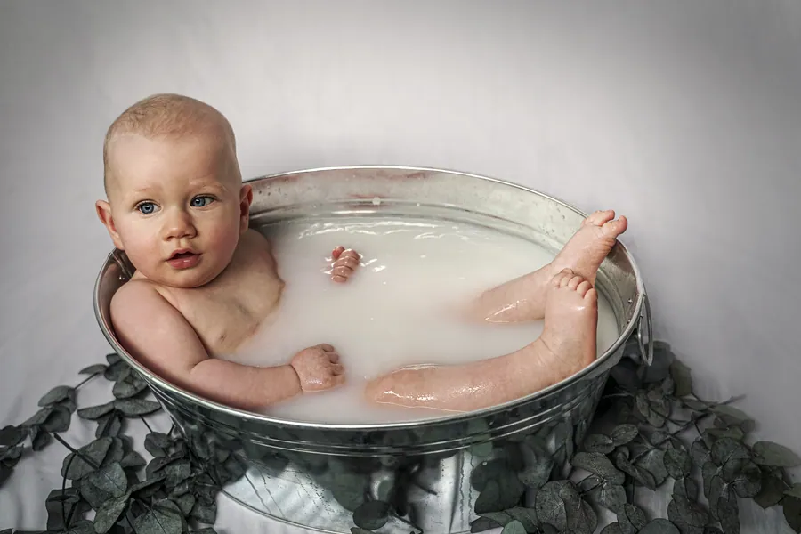 Ein Baby badet in einer Zinkwanne mit Milch und Eukalyptuszweigen