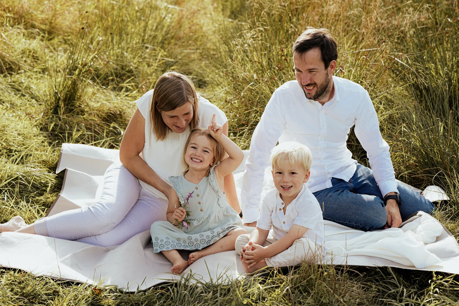 Eine Familie sitzt im Sommerlicht auf einer Decke in einer Wiese und lacht